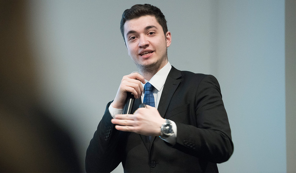 Student in a suit and tie speaking into a microphone
