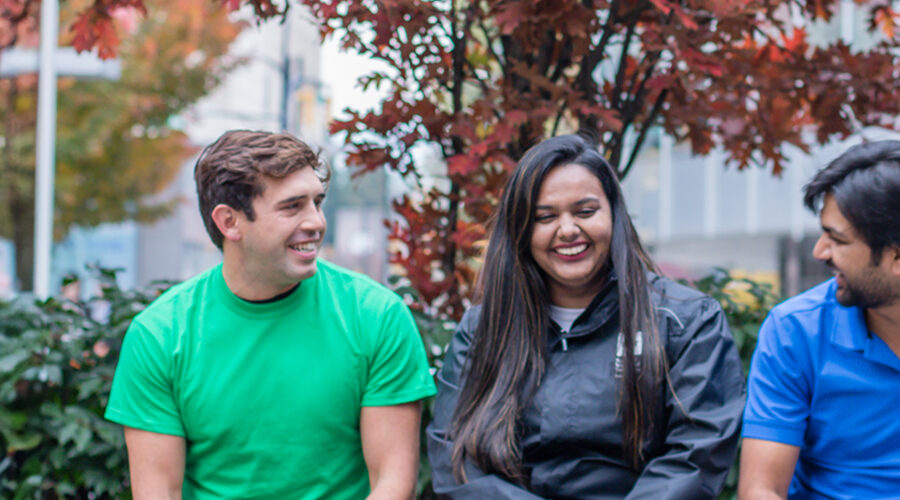 Three students chat on a bench at the Vancouver campus.