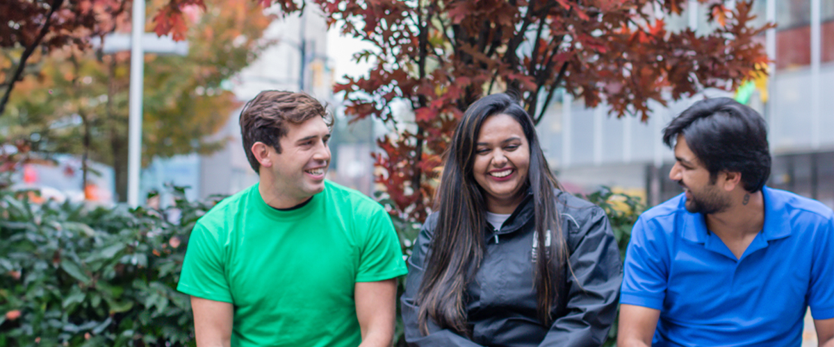 Three students chat on a bench at the Vancouver campus.