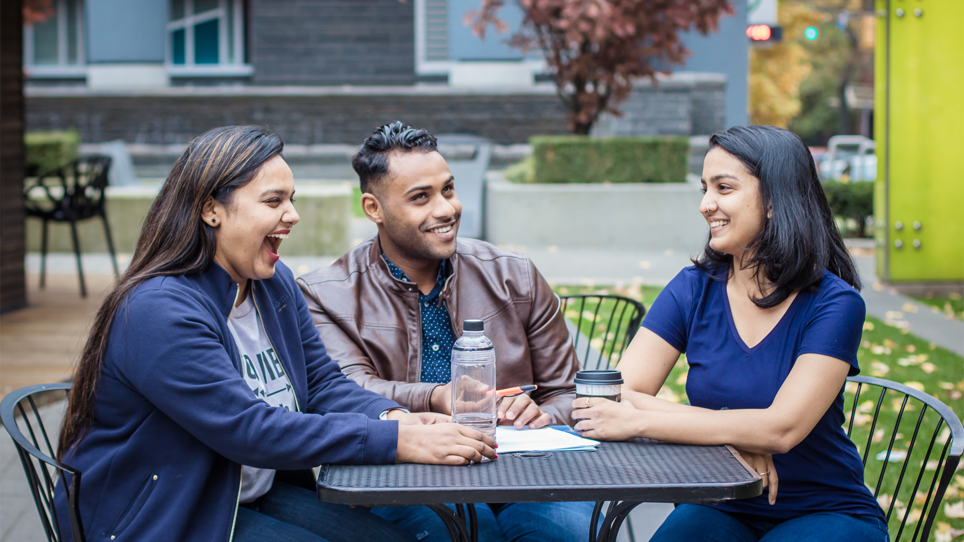 Three students converse around a table while sitting outside of New York Tech's Vancouver Campus.