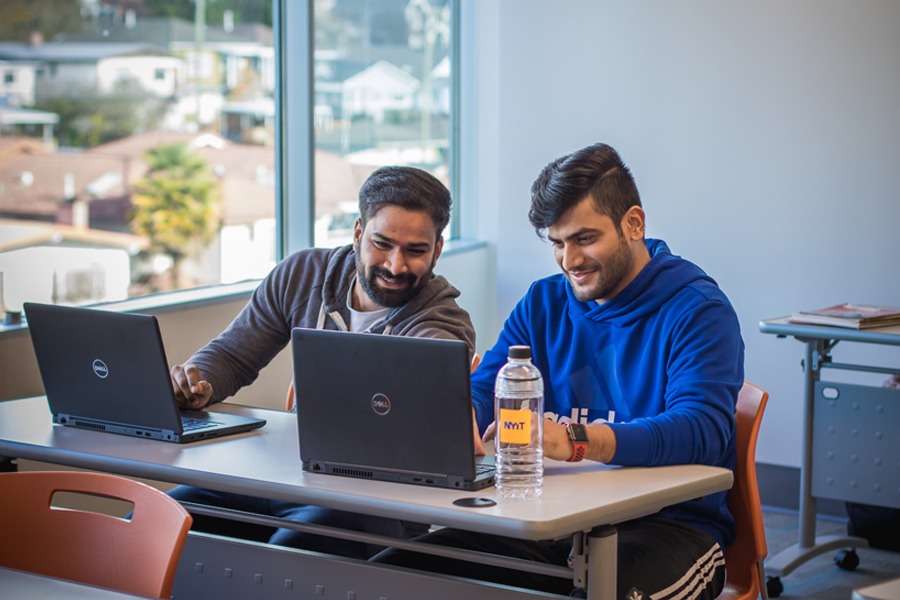 Students work together with two laptops on a table.