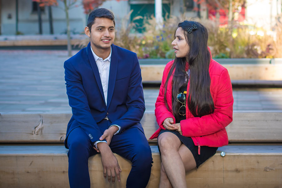 Two students are sitting on a bench outside discussing their courses. 