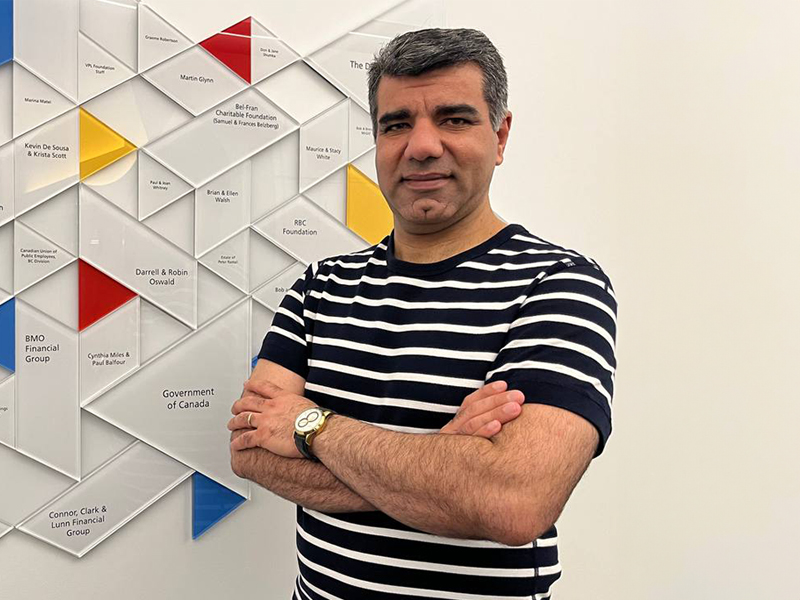 Alumnus Hassan Bakhshi stands in front of a geometric wall display inside New York Tech's Vancouver Campus.